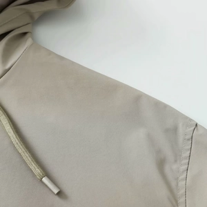 Close-up of khaki hooded jacket featuring premium stitching and woven drawstring with metal tips