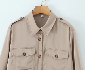 Close-up of beige satin shirt featuring classic lapels and flap pockets with buttons