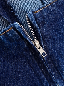 Détail macro du zip en métal argenté et surpiqûres orange sur robe en jean bleu foncé