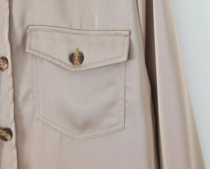 Detailed view of satin shirt pocket with amber textured resin button and neat stitching