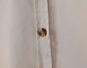 Close-up of beige satin shirt fabric with vertical texture and tortoise button detail