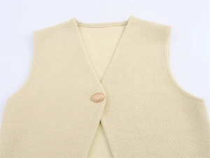 Detail of V-neck knit vest with a textured cream fabric and decorative golden button