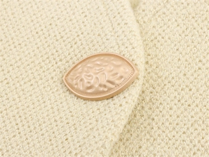 Detailed close-up of champagne gold hammered metal button on a beige knitted vest