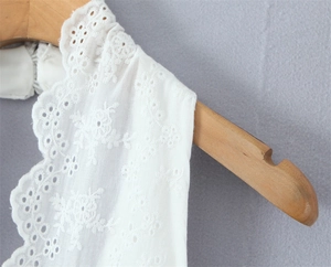 Close-up of white lace embroidery with delicate floral eyelet patterns on a wooden hanger