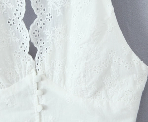 Detail of white deep V-neck top with floral embroidery and fabric covered buttons
