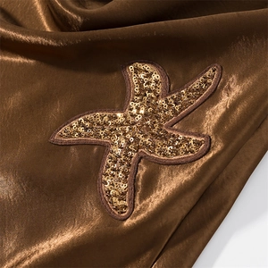 Macro detail of gold sequin starfish embroidery on sleek brown satin fabric