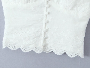 Close-up of white eyelet embroidery cotton top with fabric buttons and wavy hem