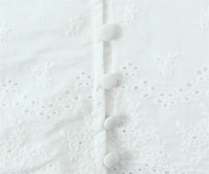 Close-up of white cotton lace top featuring eyelet embroidery and fabric-covered buttons