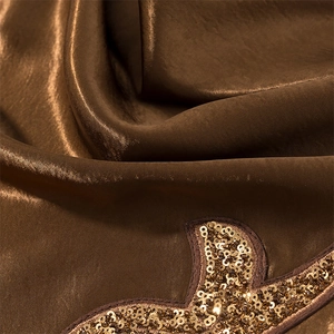 Detail of shimmering brown satin fabric with gold sequin embroidery on summer mini dress