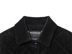 Detail of diamond quilted texture and collar on a black corduroy jacket with logo label