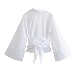 Detail of white poplin shirt with lapel collar, wide sleeves, and waist tie-up bow