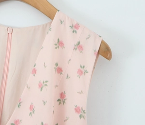 Detail of pink floral dress featuring V-neckline and concealed zipper on wood hanger
