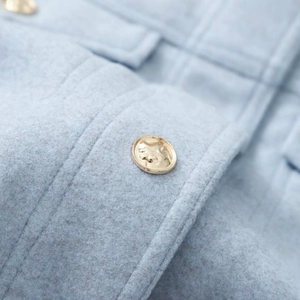 Macro shot of light blue wool blend fabric and a textured vintage gold metal button