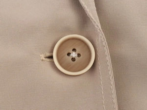 Macro detail of a beige blazer's four-hole resin button and fine twill fabric texture