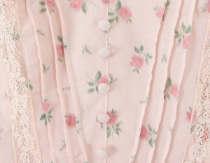 Detail of pink floral dress featuring delicate lace trim, pleats, and fabric buttons
