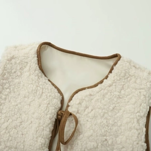 Detail of cream fleece vest featuring brown contrast piping and bow tie neck closure