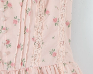 Detail of pink floral dress featuring white lace trim, fabric buttons, and pleated textures