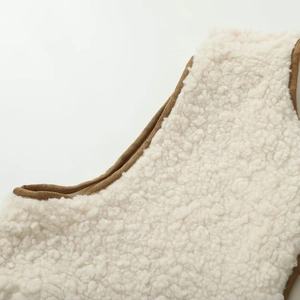 Close-up of cream fleece vest featuring brown suede piping and precise stitching detail