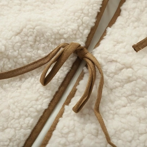 Macro detail of white fleece vest featuring brown suede piping and decorative ribbon tie