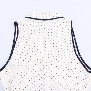 Detailed back view of sleeveless white polka dot blouse with navy blue contrast piping
