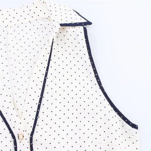 Detail of white sleeveless polka dot blouse with black trim and elegant gold button