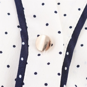 Close-up of white polka dot fabric with a glossy gold metal button and contrast binding