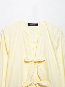 Detail of light yellow striped shirt featuring a v-neck and bow with zigzag stitching