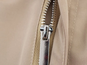 Detailed close-up of a high-quality silver metal zipper on khaki twill blazer fabric