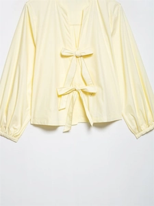 Detail of yellow striped shirt showing decorative bows and delicate zigzag stitching