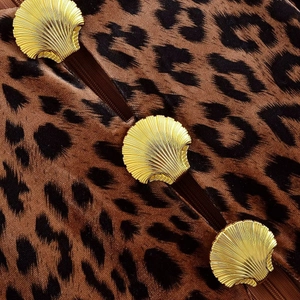 Detailed macro view of leopard print velvet fabric with golden shell-shaped metal buttons