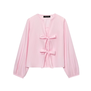 Detail of pink long sleeve blouse featuring decorative bows and a subtle V-neckline