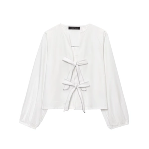 Detail of white long sleeve top featuring stylish bow tie closures and V-neckline