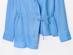Close-up of sky blue wrap shirt showing linen texture and tie-waist detail