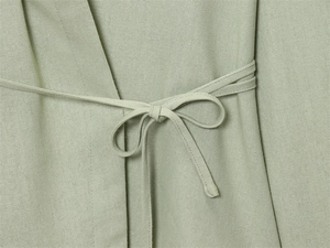 Detailed close-up of light green linen fabric texture with a waist tie bow detail