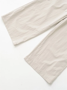Detail of light beige wide-leg trousers showing natural crinkle texture and premium fabric