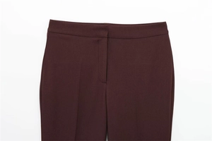 Detail of high-waist wine red trousers featuring a concealed zipper and pressed crease