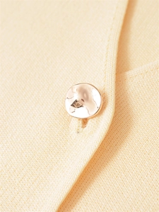 Detailed close-up of a golden textured metal button on cream knit pullover fabric