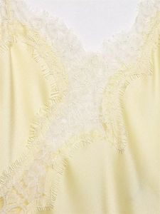 Detail of light yellow satin camisole with delicate white eyelash lace trim on the neckline