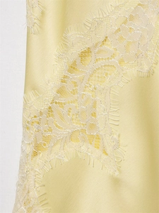 Detailed close-up of light yellow satin fabric with delicate white floral lace trim