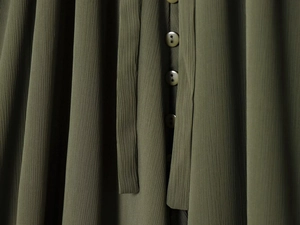 Detailed macro view of army green crepe fabric texture and round buttons on long sleeve shirt