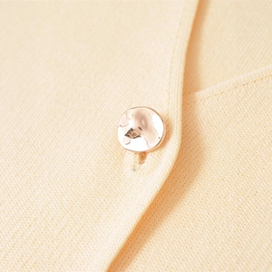 Minimalist knit sweater featuring a polished rose gold button on cream fabric texture