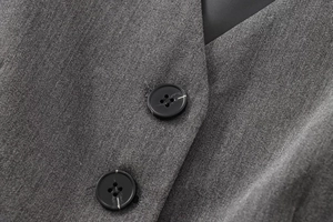 Gros plan sur la texture du tissu sergé gris foncé et les boutons en résine noire d'un gilet
