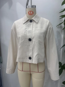 Detail of beige cropped jacket with contrasting black buttons and large front pockets