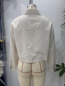 Detail of beige cropped jacket back featuring horizontal seam and buttoned cuffs