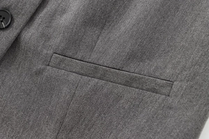 Détail de la texture du tissu gris du gilet avec bouton et poche passepoilée