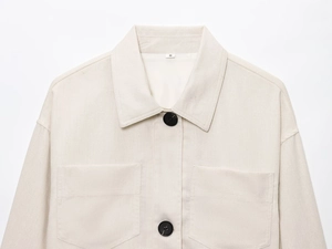 Detail view of beige shirt jacket with classic collar, large black buttons and chest pockets