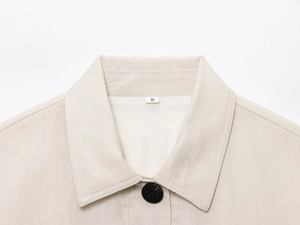 Close-up of linen fabric texture, notch lapel and black button detail on beige jacket