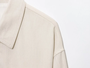 Close-up detail of cream cropped jacket showing lapel collar and woven linen texture