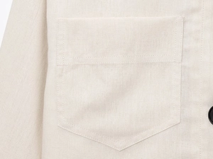 Macro detail of a beige linen jacket showing stitched patch pocket and a black button