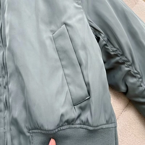 Macro detail of sage green satin bomber jacket with side pocket and ribbed hem finish